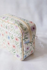 Floral-patterned toiletry bag with white baby ric rac on a white background