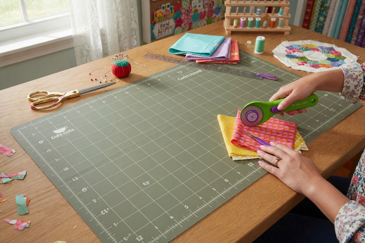 Person cutting fabric with a rotary cutter on a cutting mat in a craft room.
