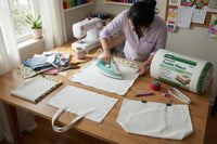 Person ironing fabric on a table with sewing supplies in a home setting